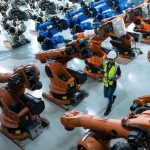 a-female-engineer-installs-a-program-on-a-robotics-arm-in-a-robot-warehouse-.jpg